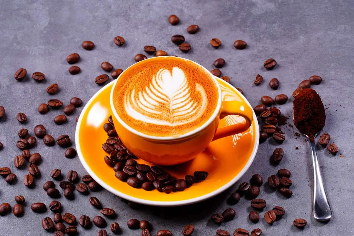 A cappuccino on an orange saucer with coffee beans